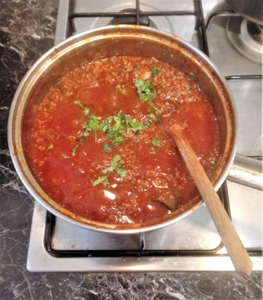 A saucepan of Italian ragu alla bolognese being mixed on an electric hob with a wooden spoon.