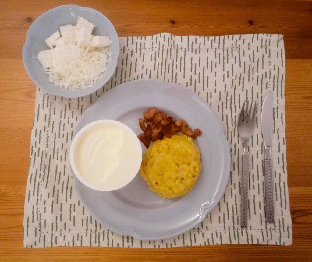 Moldovan mamaliga polenta and bacon  jumari with sour cream and goats' cheese, served on blue crockery, green and white place mat and wooden table with metal cutlery