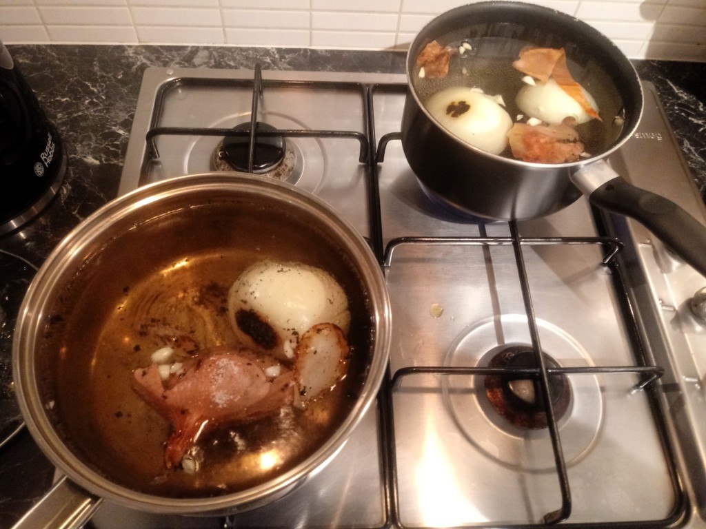 Two metal saucepans pans of burning onions, onion skin and water on a metal Smeg gas hob with a Russell Hobbs kettle