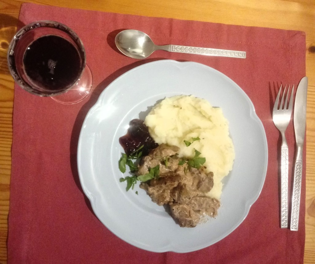 Finnish poronkaristys served on a blue plate and red tablecloth with metal cutlery and a glass of red grape juice