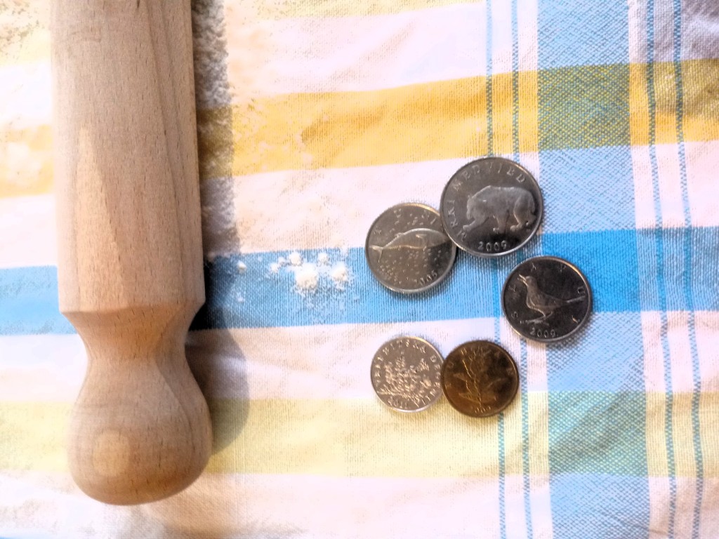 Croatian coins on a blue, yellow and white tea-towel with flour and a wooden rolling pin
