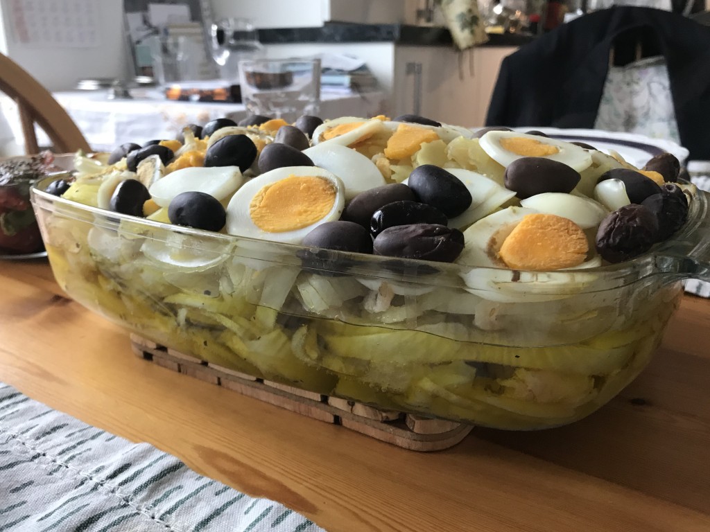 Portuguese bacalhau side on in a transparent ovenproof dish with side salad on a wooden table mat with green and white place mats against a kitchen backdrop